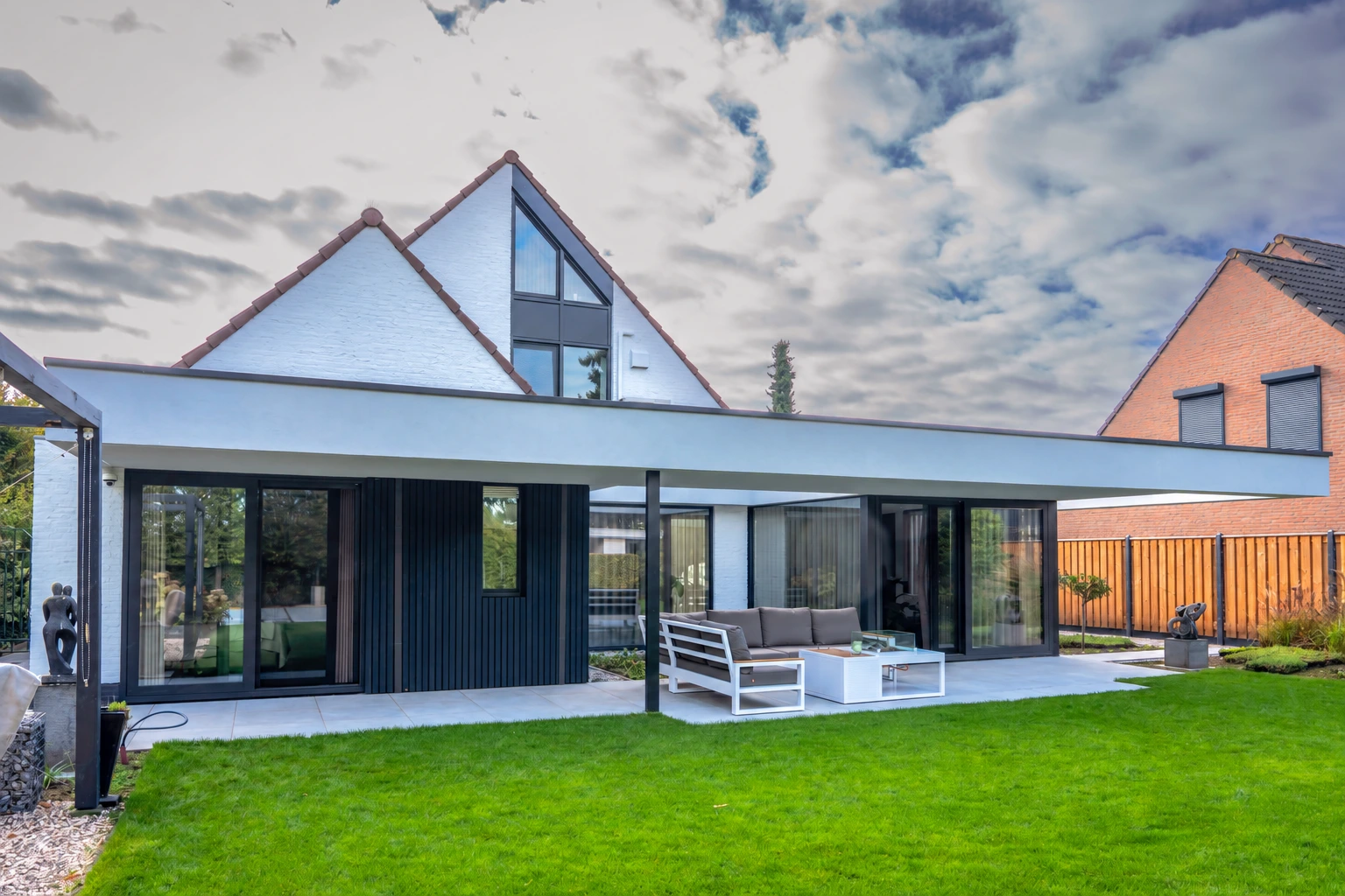 De verbouwde woning in Heythuysen met twee witte topgevels, een overdekt terras en groene tuin